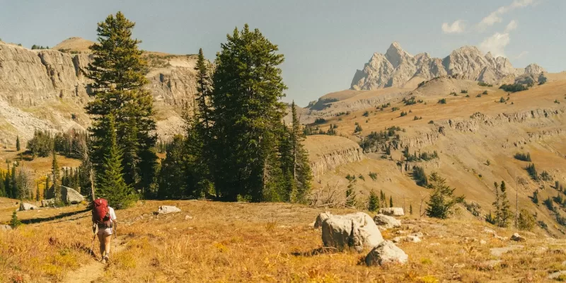 Hiker with backpack walks on a trail in the mountains.